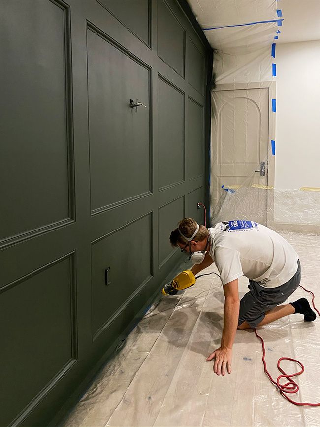 a man in white shirt and black shorts working on a wall with paint rollers