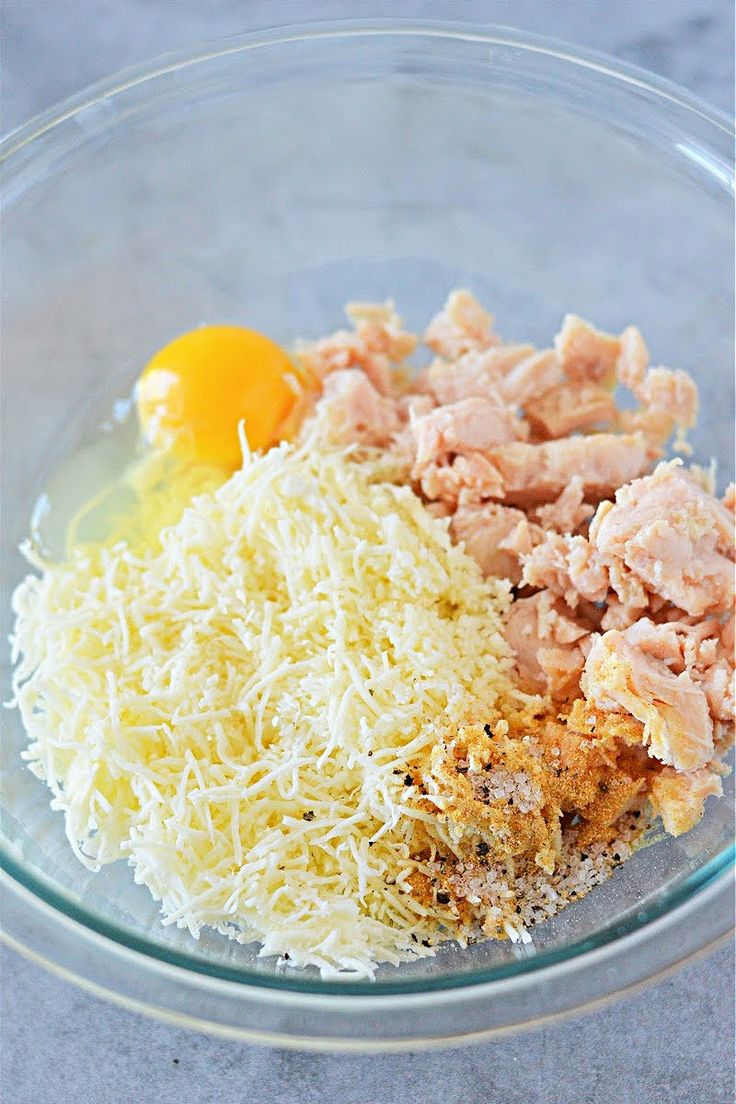 the ingredients for this dish are in a glass bowl, including shredded cheese and an egg