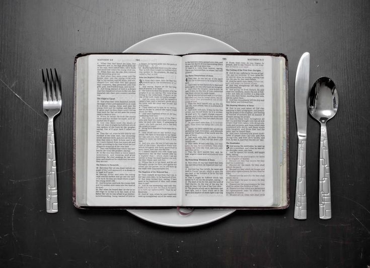 an open book sitting on top of a table next to two forks and spoons