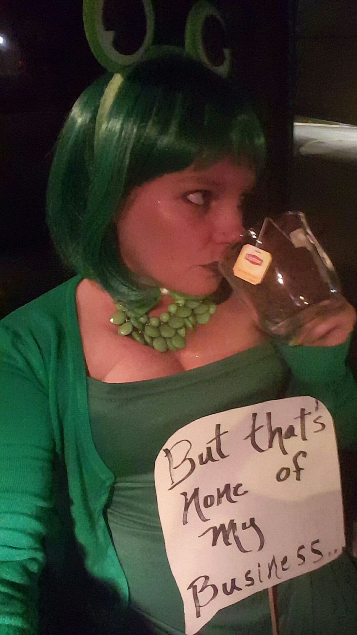 a woman with green hair drinking from a wine glass and holding a sign that says, but that's none of my business