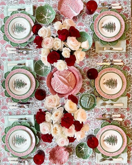 the table is set with pink and green plates, silverware, and red flowers