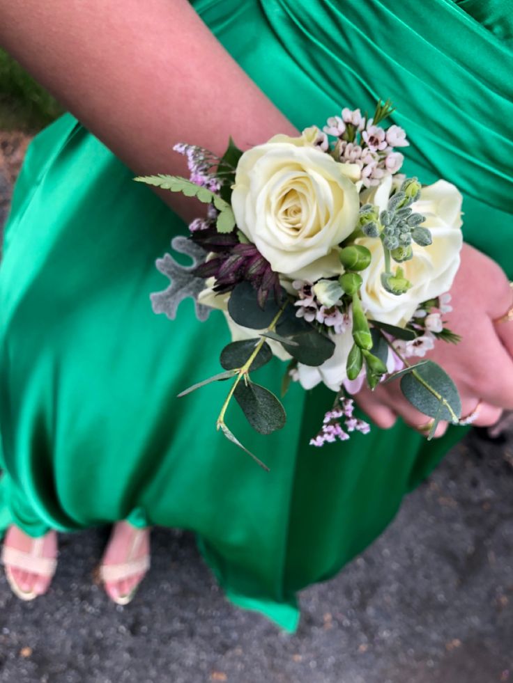 a woman in a green dress holding a white rose and greenery corsage