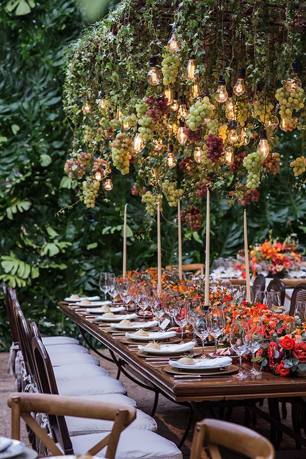 an outdoor dining table set up with candles and flowers in the center, surrounded by greenery