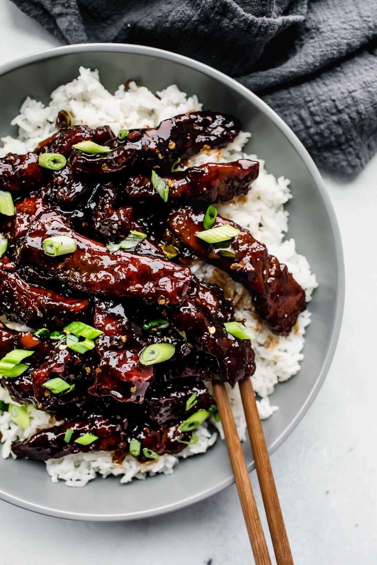 a bowl filled with rice and meat on top of a white table next to chopsticks