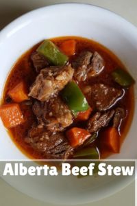 a white bowl filled with beef stew and carrots on top of a wooden table