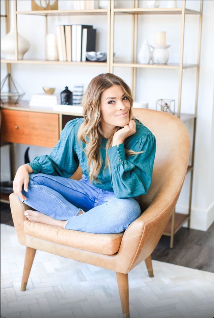 a woman sitting in a chair with her hand on her chin and looking at the camera