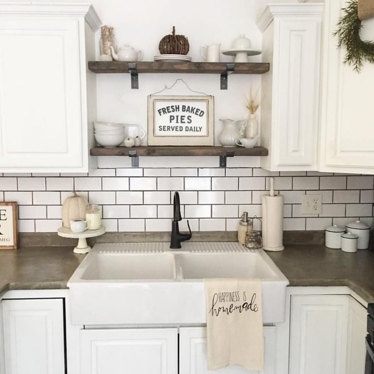 a kitchen with white cabinets and tile backsplash, christmas wreath on the shelf above the sink