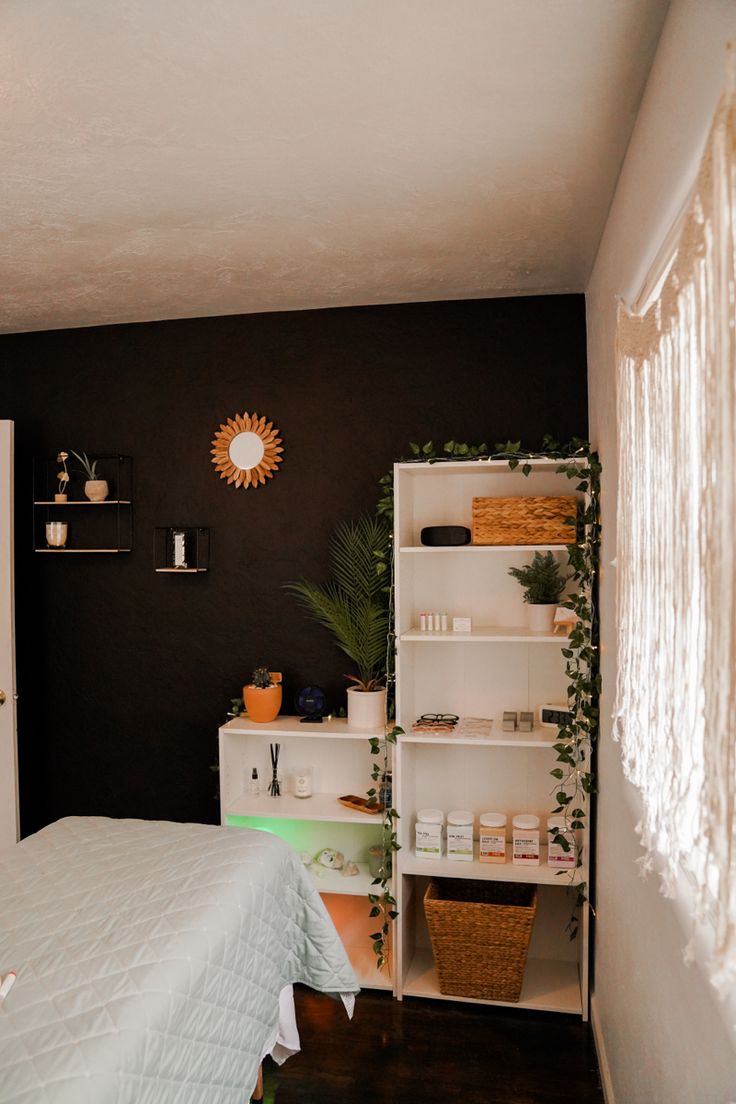 a bedroom with black walls, white bedding and shelves filled with plants on the wall