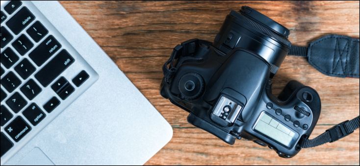 a laptop computer sitting on top of a wooden table next to a camera and flash drive