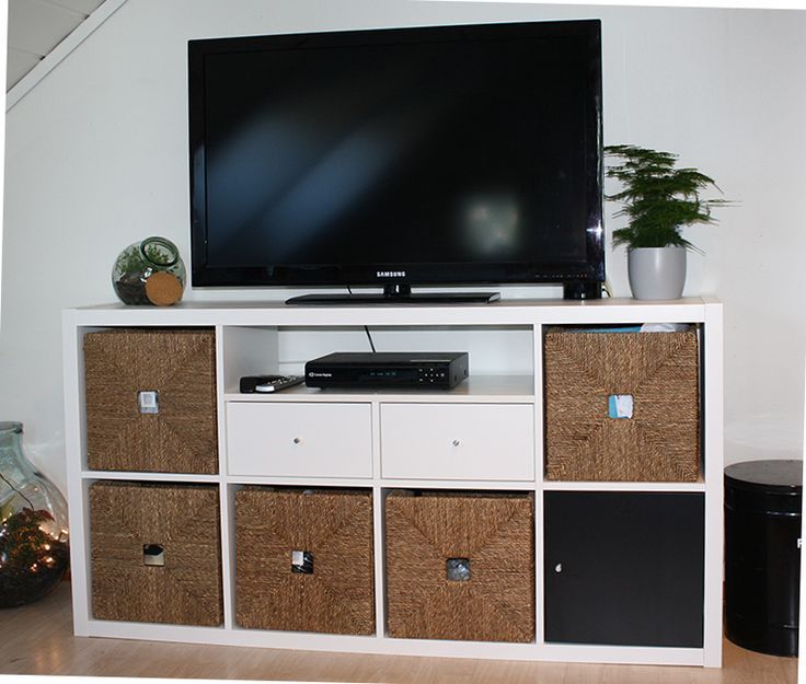 a flat screen tv mounted on top of a white entertainment center with baskets underneath it