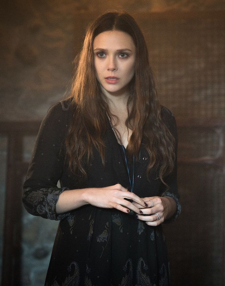 a woman with long hair standing in front of a wall and looking at the camera