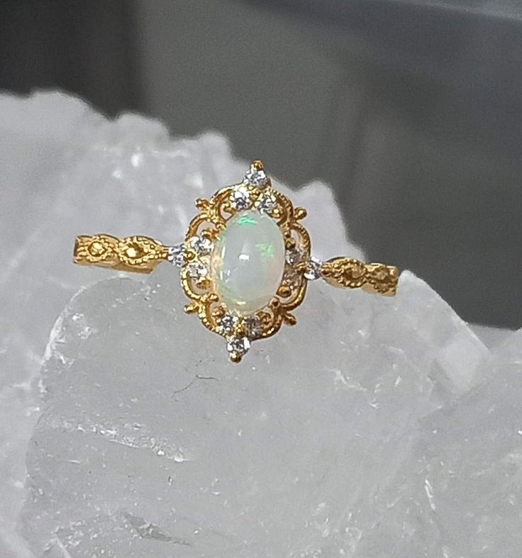 This solid gold beautiful vintage-style natural opal ring is a true statement piece that is sure to be noticed and admired. It is the perfect ring for an evening out on the town, prom, wedding, or special occasion. Our opal ring features solid 14k or 18k yellow gold, rose or white gold and is accented with gorgeous simulated diamonds that shimmer in the light. It makes a fine gift or an excellent addition to your collection. The opal stone is cut in a oval shape. It is meticulously set with an e Natural Opal Ring, Cute Engagement Rings, Opal Wedding Rings, Engagement Ring For Women, Opal Ring Gold, Engagement Rings Opal, Knot Ring, Solid Gold Jewelry, October Birthstone