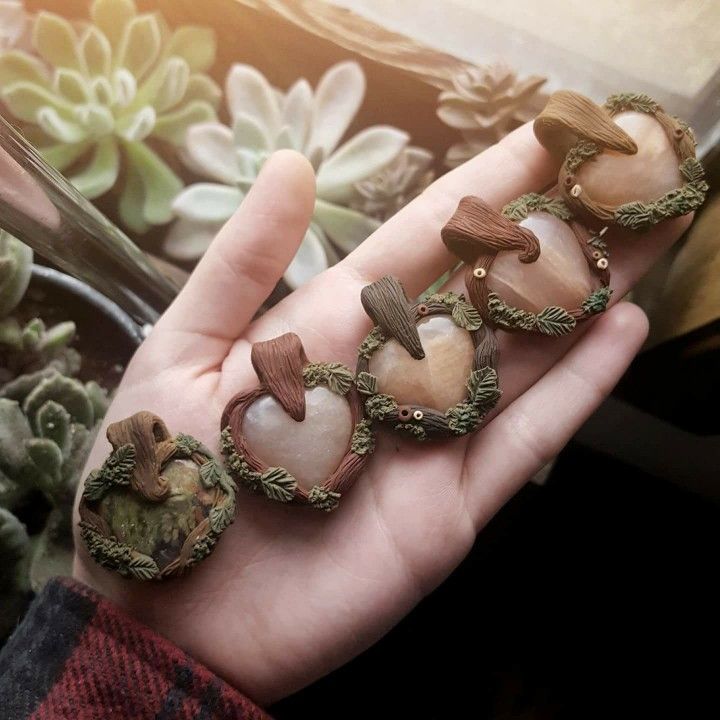 a hand holding five different shaped rocks in front of some succulents