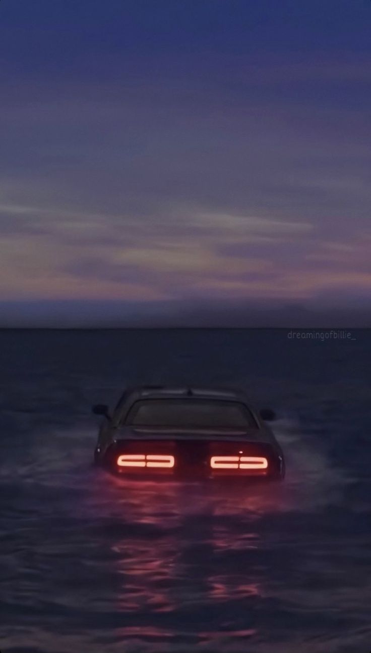 a car that is sitting in the water with its headlight turned on at night