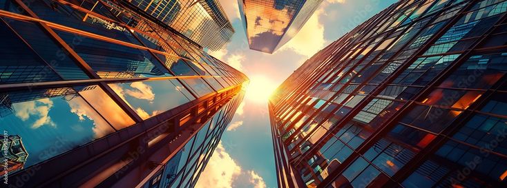 looking up at skyscrapers from the ground to the sky with clouds and sun shining through them