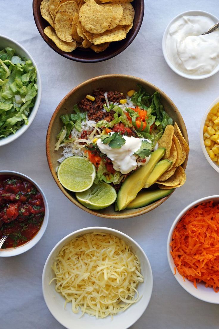 bowls filled with different types of food on top of a white table covered in condiments