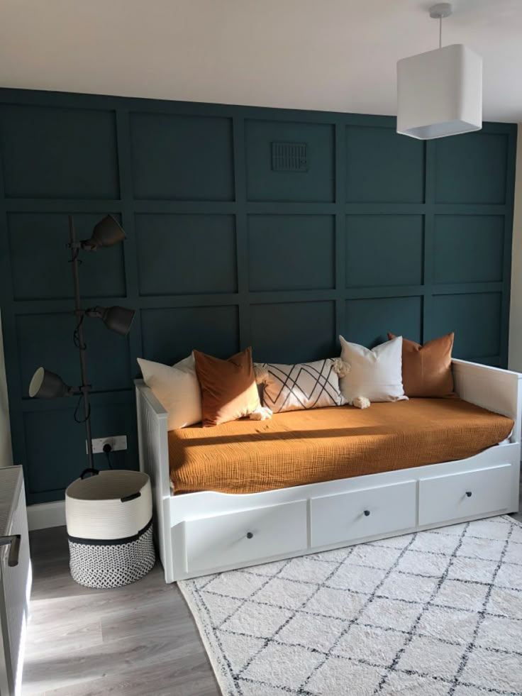 a bed with lots of pillows on top of it in front of a blue wall