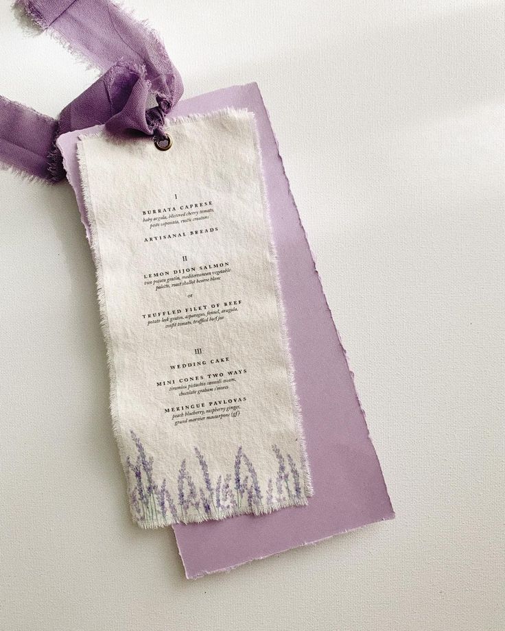 a purple and white wedding menu with ribbon on it's neckline, sitting on top of a table