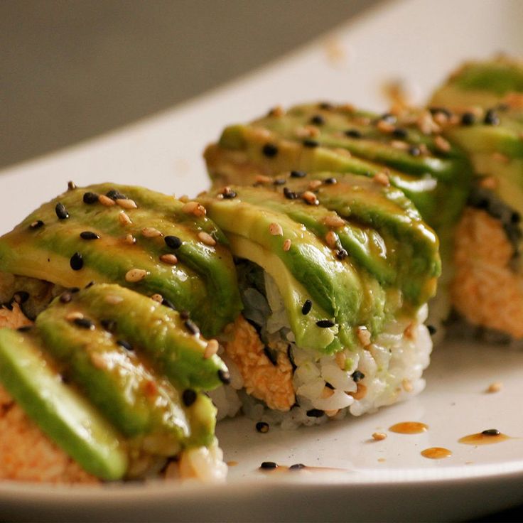 sushi rolls covered in green sauce and sesame seeds