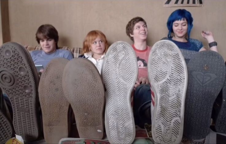 four people are sitting in front of several pairs of shoes that look like they have their feet up