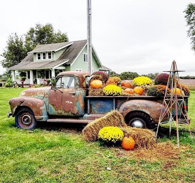 an old truck with hay and pumpkins on the back in front of a house