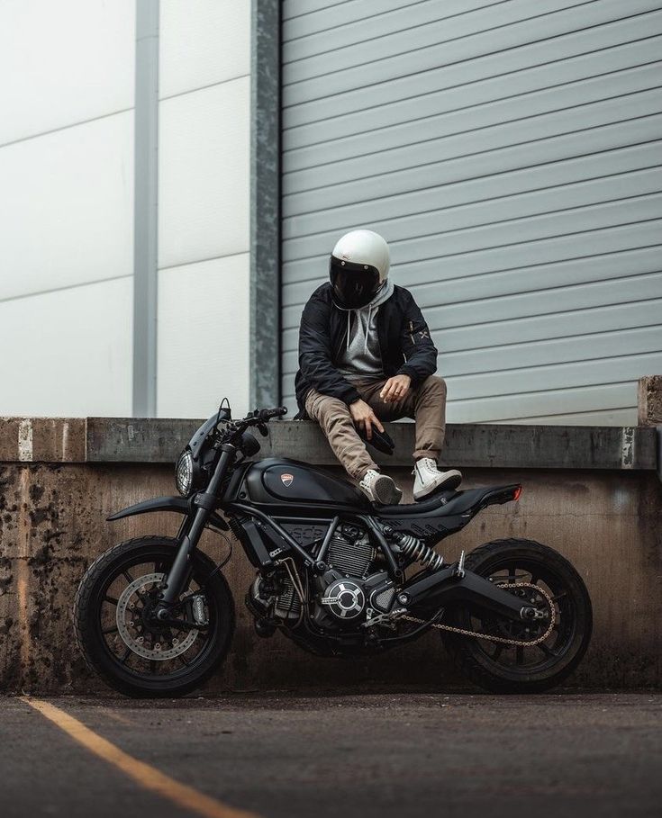 a man sitting on the back of a motorcycle next to a garage door and wearing a helmet