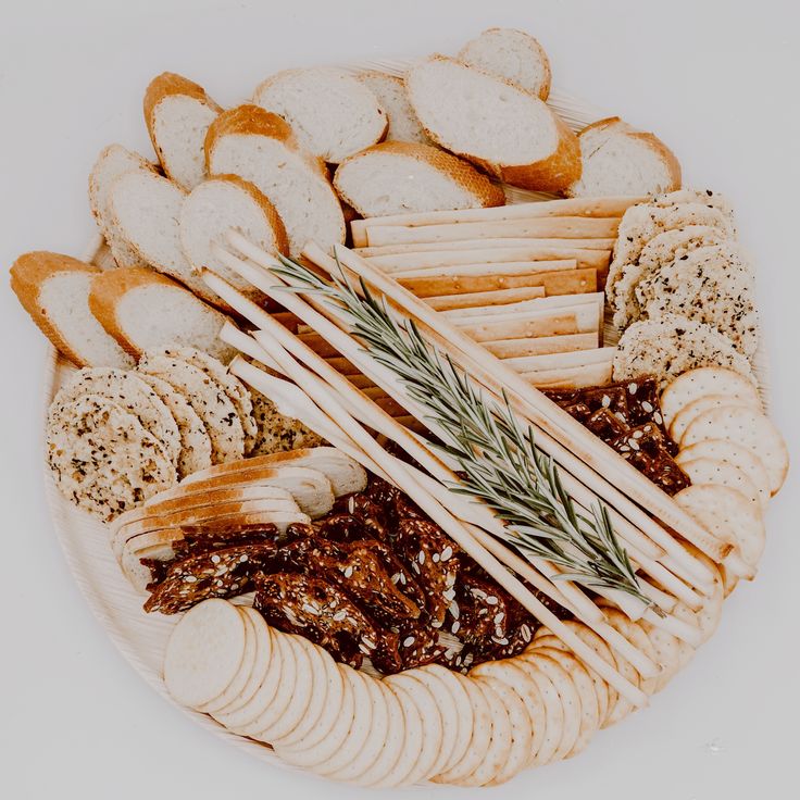 an assortment of breads and crackers on a platter with rosemary sprigs