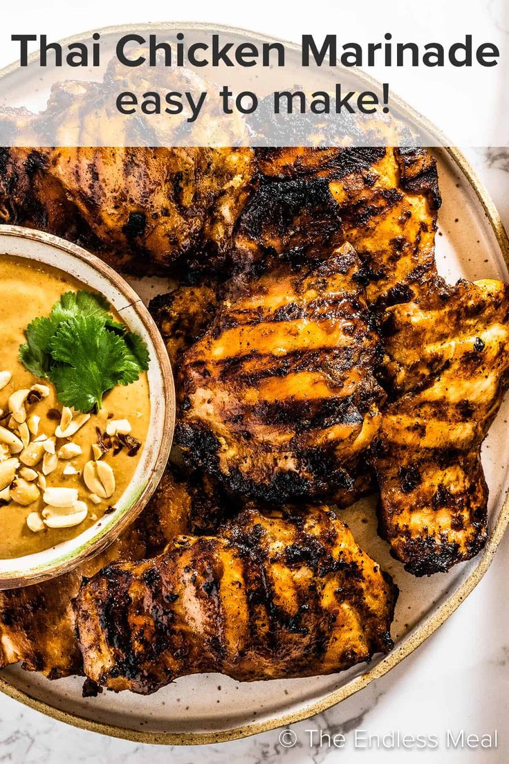 grilled chicken on a plate with a bowl of peanut sauce and garnish