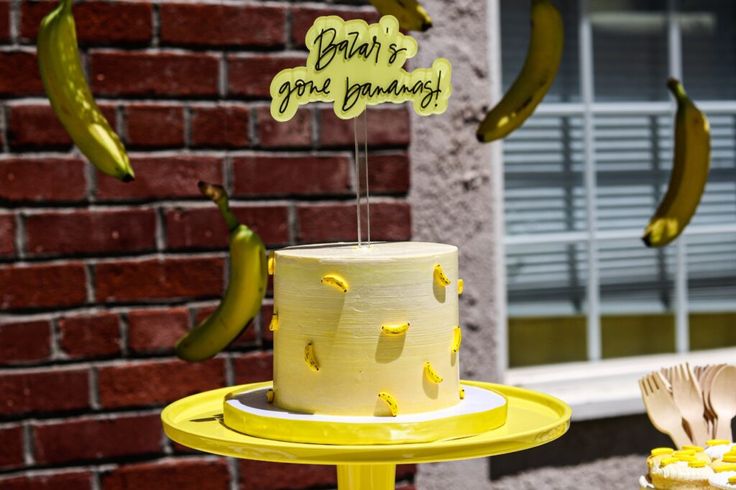 a yellow cake sitting on top of a table with bananas hanging from it's sides