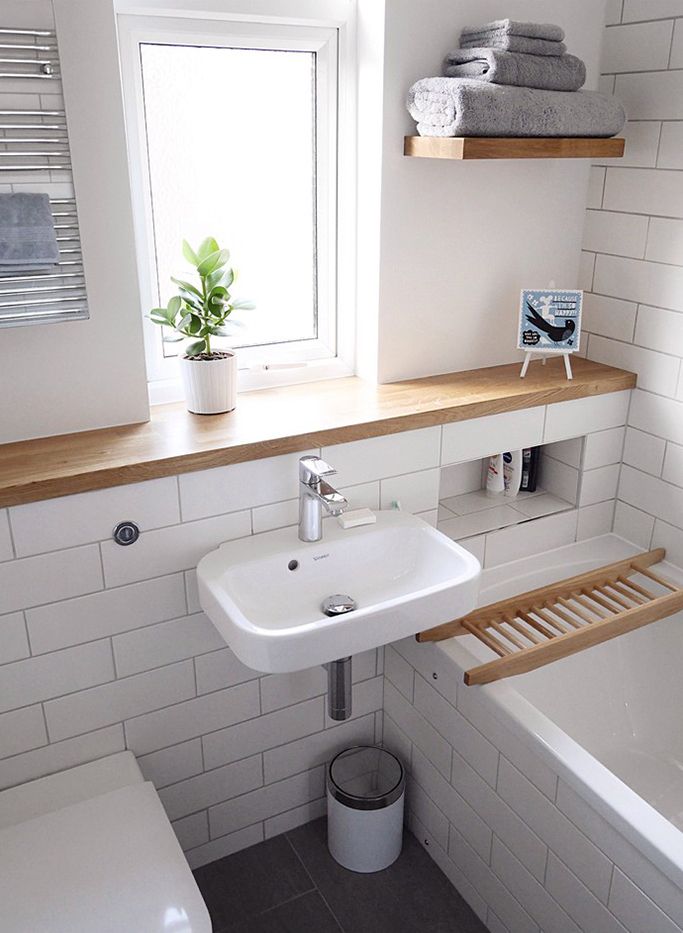 a small bathroom with white tile and wood shelves above the toilet, sink, and bathtub