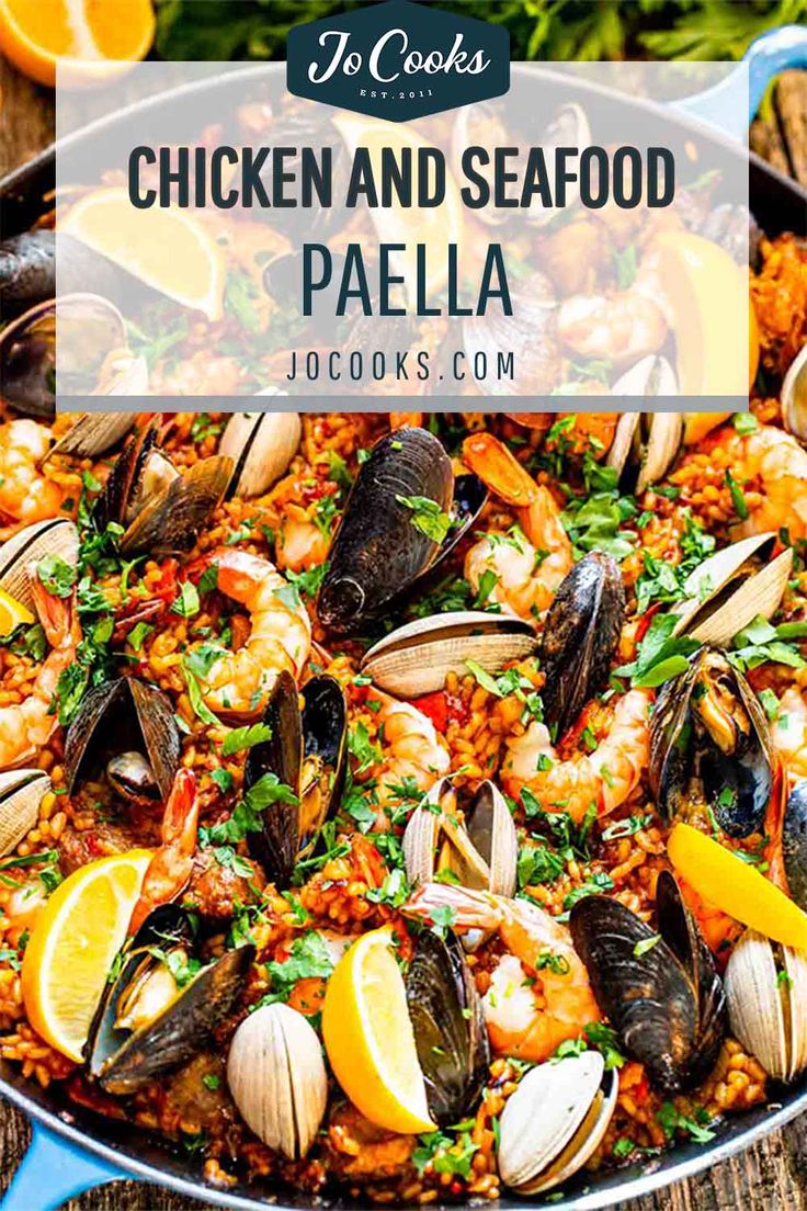 chicken and seafood paella in a pan with lemon wedges