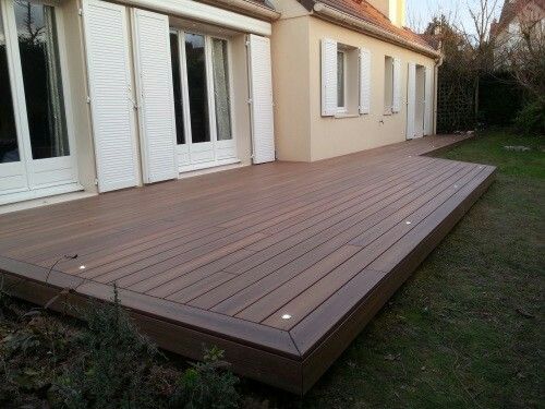 a wooden deck in front of a house with white shutters and sliding glass doors