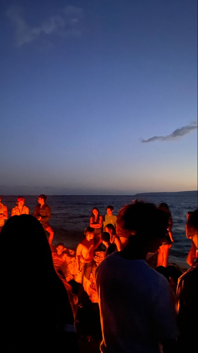 a group of people sitting around a campfire on the beach at night with bright lights