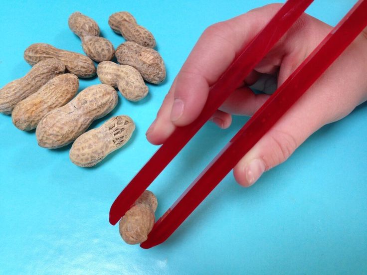 a hand holding chopsticks over peanuts on a blue surface with red plastic handles