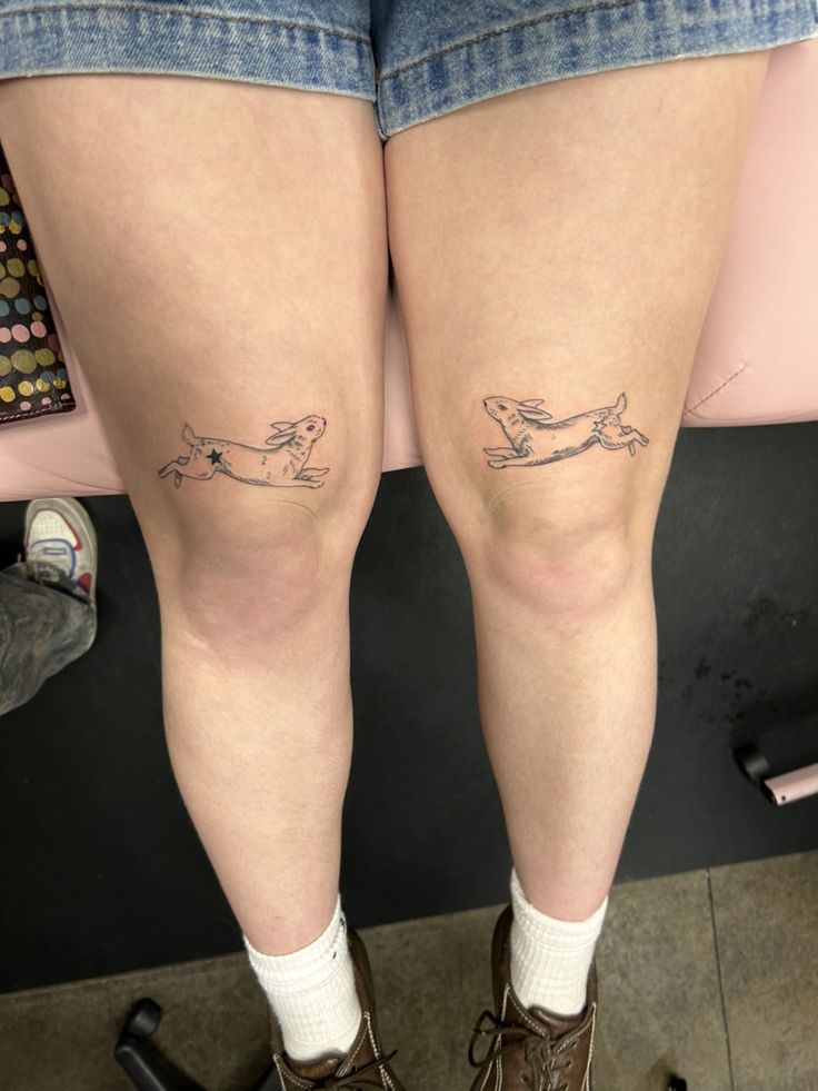 Two Bunny knee Tattoo Black Ink Asymmetrical Above The Knees Tattoos, Nastolgia Tattoo, Matching Above Knee Tattoo, Tattoo Under Knee Woman, Double Knee Tattoo, Knee Tattoo Symmetrical, Tattoo Behind Knee, Word Knee Tattoos, Symmetrical Knee Tattoos