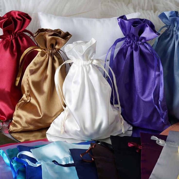 many different colored satin bags sitting on top of a white pillow with candles in them