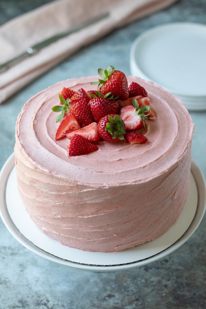 a strawberry cake with frosting and fresh strawberries on top is ready to be eaten