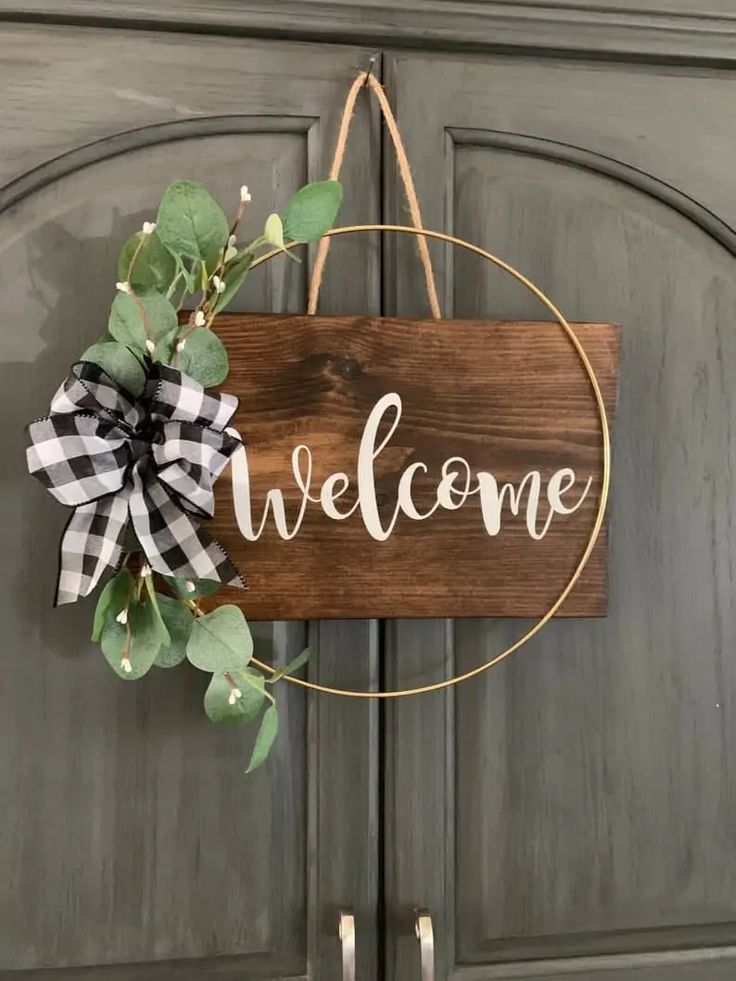 a wooden welcome sign hanging on a door with greenery and ribbon around the frame