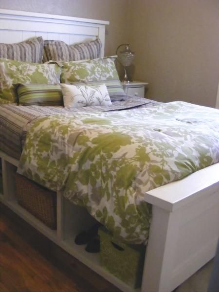 a bed with green and white bedspread, pillows and baskets on the headboard