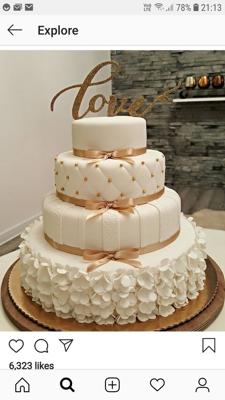 a three tiered wedding cake with white flowers and gold lettering on top, sitting on a table