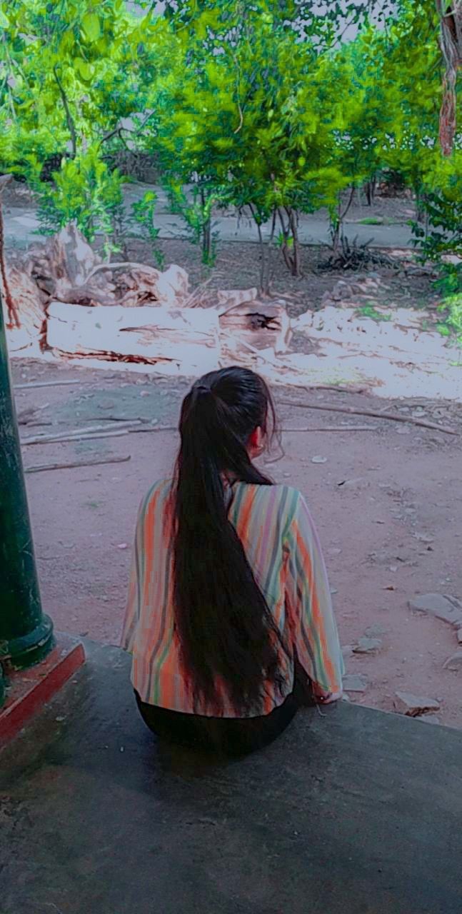 a woman sitting on the ground next to a green pole with trees in the background