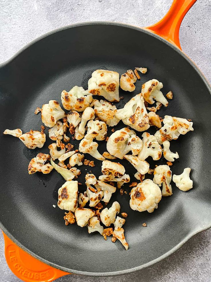 cauliflower being cooked in a frying pan on an orange spatula,