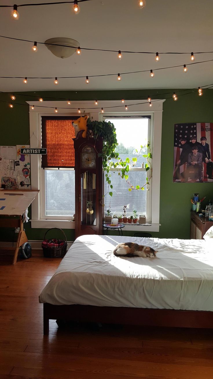 a cat laying on top of a white bed in a room with green walls and wooden floors