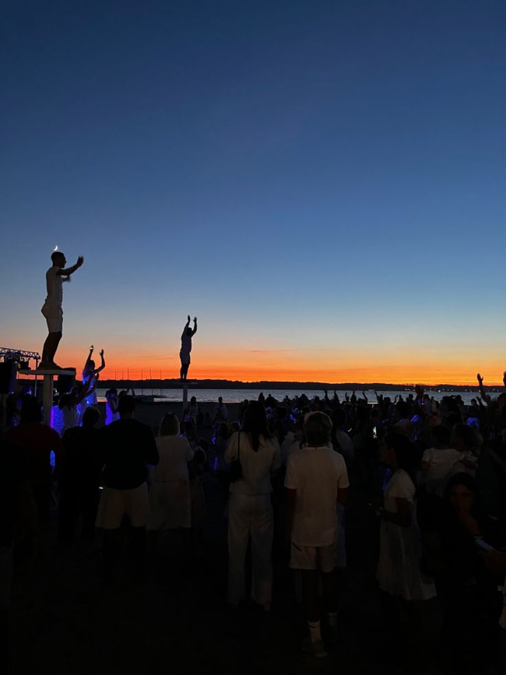 people standing around watching the sun set at an outdoor concert with one person jumping in the air