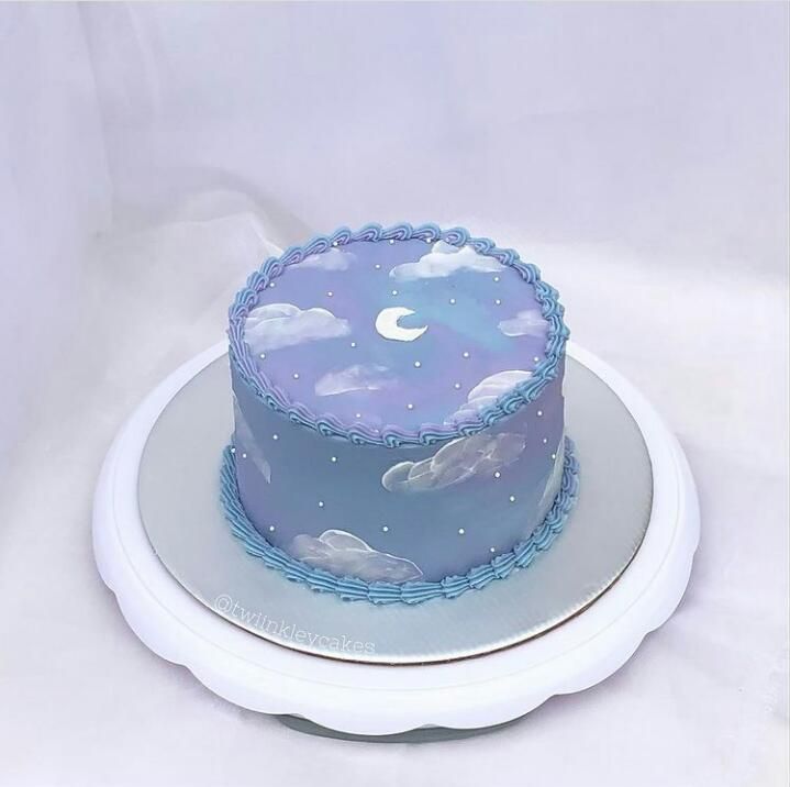 a blue cake with clouds and stars on it is sitting on a white platter