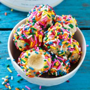 a bowl filled with sprinkle covered donuts on top of a blue table