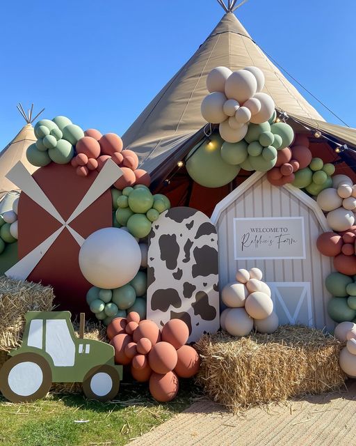 an outdoor display with hay bales, balloons and farm animals in front of a teepee tent