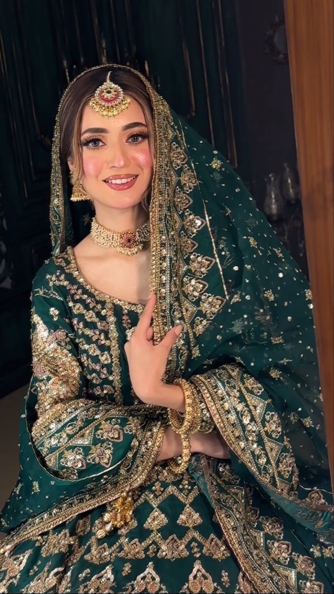 a woman in a green and gold bridal gown posing for the camera with her hands on her hips