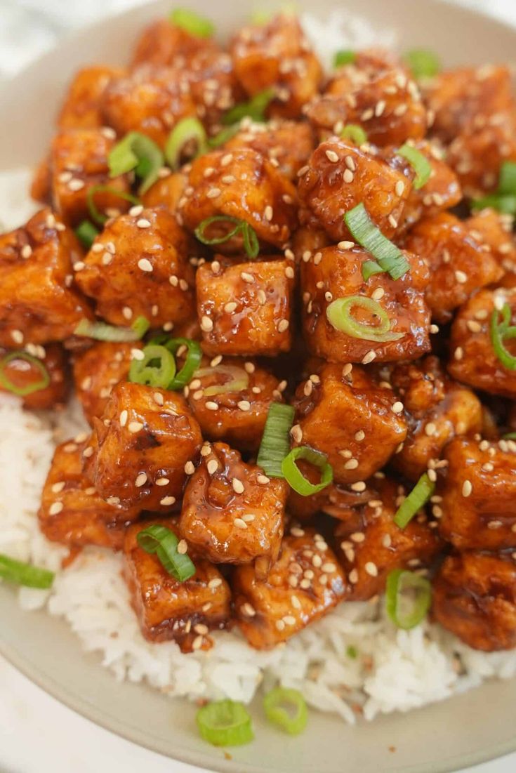 a white plate topped with chicken and rice covered in sesame seeds on top of it