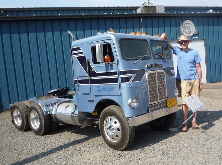 a man standing next to a large truck in front of a blue building with a flag on it